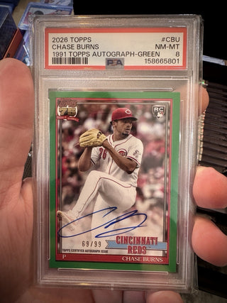 A PSA-graded 2026 Topps Chase Burns baseball autograph card, sealed in a clear plastic holder and held in a person's hand. The card features a green border, a photo of Chase Burns in a Cincinnati Reds uniform, a blue autograph, and a red PSA grading label at the top.