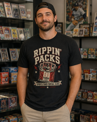 A man wearing a black graphic t-shirt with 'Rippin' Packs Sports Card Social Club' printed on the front, standing in front of shelves filled with collectible trading cards.