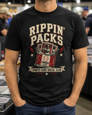 A man wearing a black graphic t-shirt with a distressed cream and red 'Rippin' Packs Sports Card Social Club' design, standing in a crowded indoor event space.